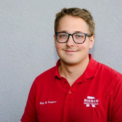 Porträtfoto von Benedict Grabner, Geschäftsführer, im roten Rieser-Poloshirt.