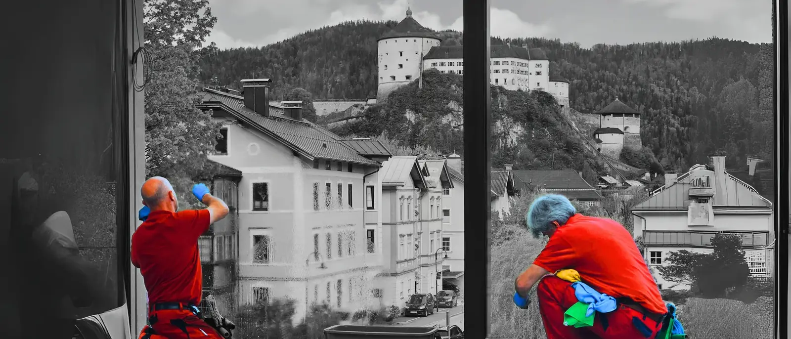 Zwei Mitarbeiter reinigen von innen eine große Fensterfront. Dahinter liegen die Dächer von Kufstein und die Festung auf dem Felsen.