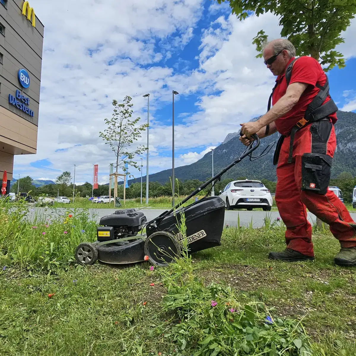Ein Mitarbeiter mäht eine Grünfläche vor einem Hotel. Im Hintergrund liegen das Inntal und die Berge.