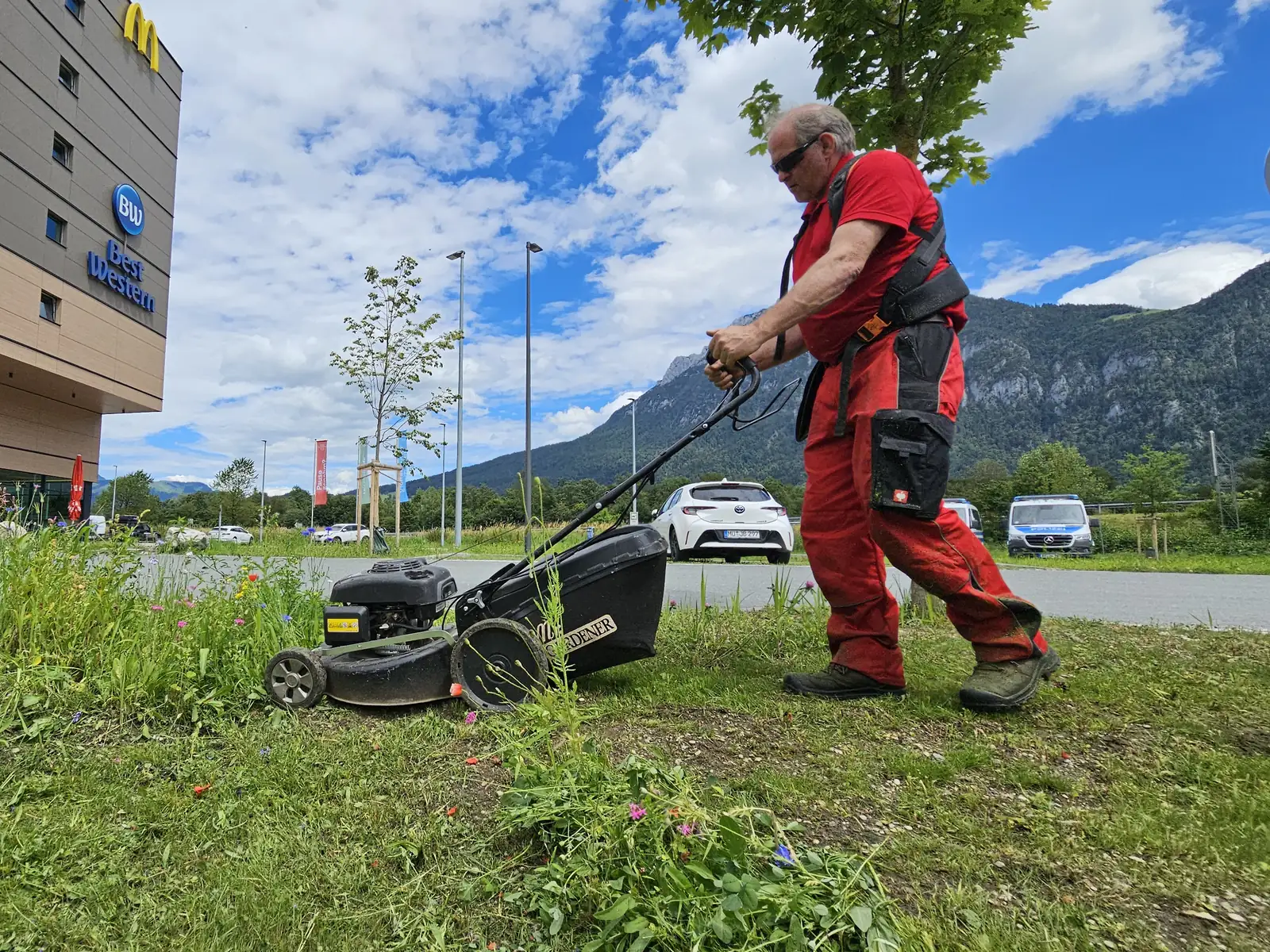 Ein Mitarbeiter mäht eine Grünfläche vor einem Hotel. Im Hintergrund liegen das Inntal und die Berge.