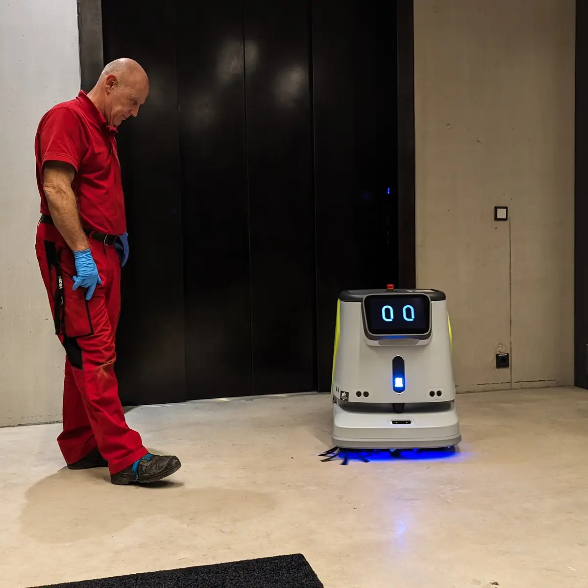Ein Mitarbeiter steht in einer Lobby neben einem weißen Reinigungsroboter mit beleuchtetem Display.