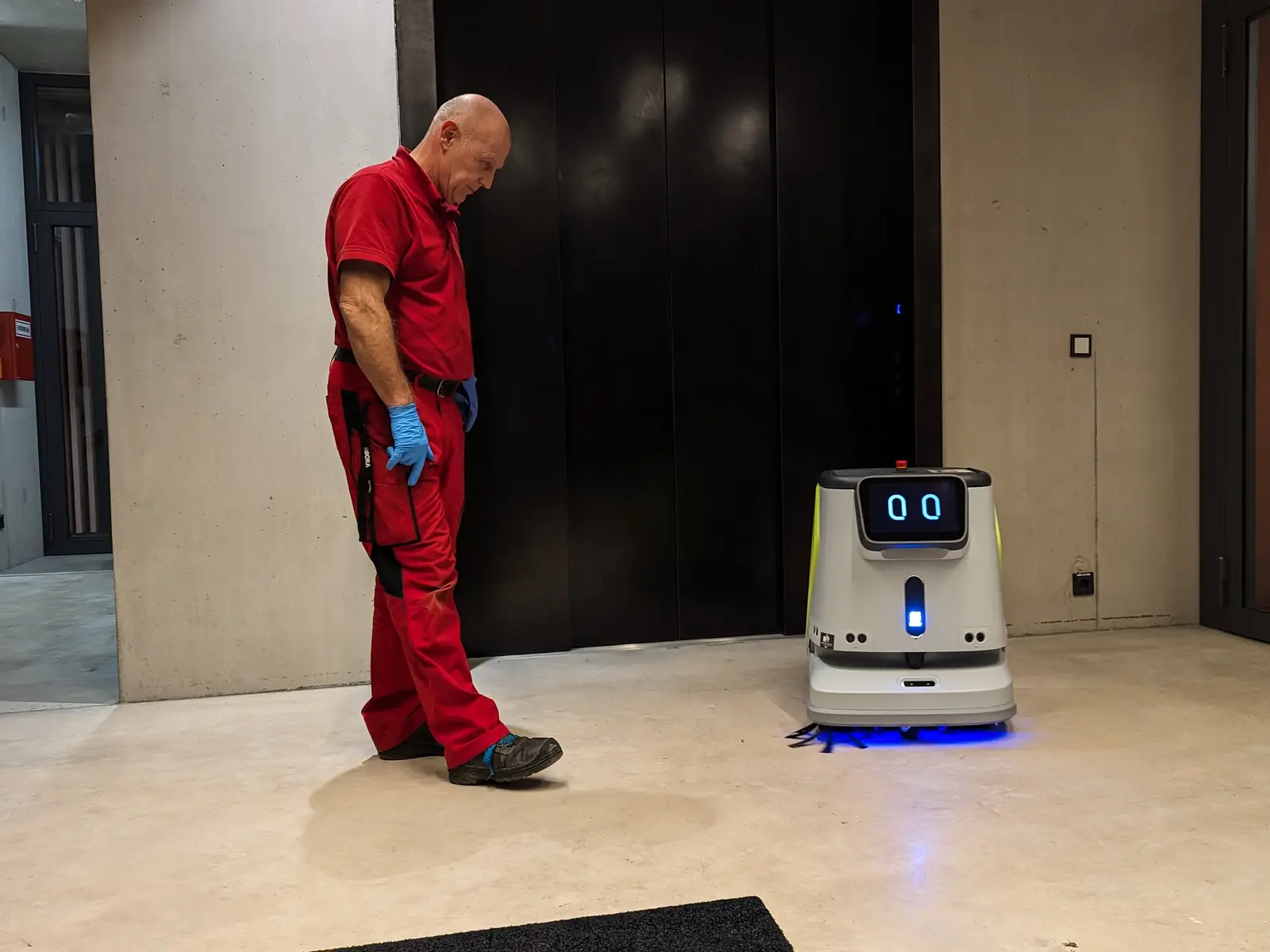 Ein Mitarbeiter steht in einer Lobby neben einem weißen Reinigungsroboter mit beleuchtetem Display.