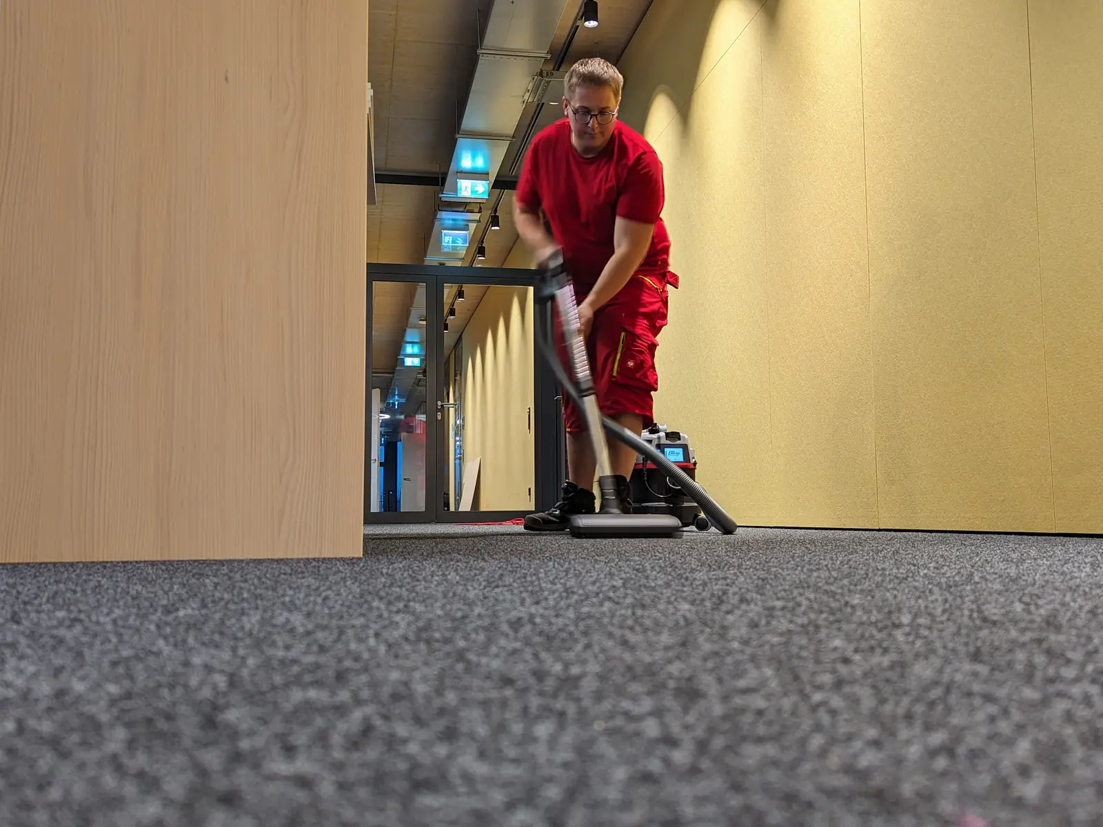 Mitarbeiter saugt den Teppichboden in einem Großraumbüro. Die Aufnahme ist dicht über dem Boden gemacht.